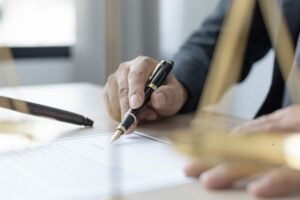 Dettaglio di un braccio con cravatta che scrive e un contratto con penna stilosa.