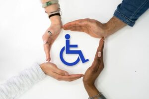 Quattro mani di persone diverse per età e carnagione formano un cerchio protettivo attorno al simbolo della disabilità, esprimendo inclusione, sostegno e solidarietà.