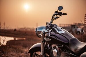 Moto custom parcheggiata su un terreno all’aperto al tramonto, con il sole basso sull’orizzonte e una luce calda che avvolge il paesaggio rurale sullo sfondo.