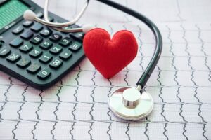 Stetoscopio, calcolatrice e cuore rosso su un tracciato elettrocardiografico: simbolo del legame tra salute, prevenzione e gestione dei costi sanitari