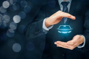 Concetto di assicurazione auto: uomo in abito elegante protegge con le mani un’icona luminosa di automobile, su sfondo scuro sfocato.