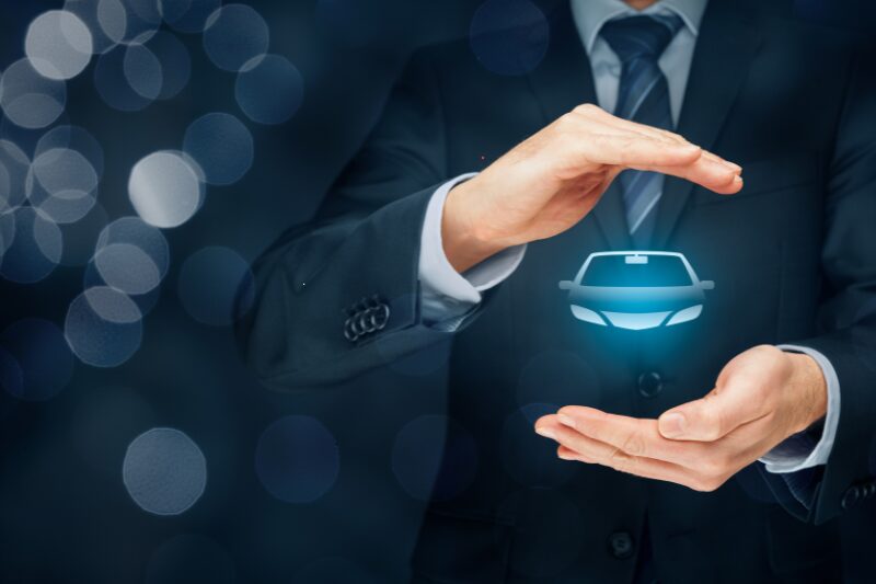 Concetto di assicurazione auto: uomo in abito elegante protegge con le mani un’icona luminosa di automobile, su sfondo scuro sfocato.