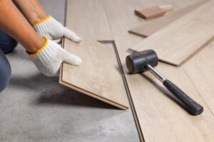 Persona con guanti da lavoro che posa un pavimento in legno durante la ristrutturazione di una casa.