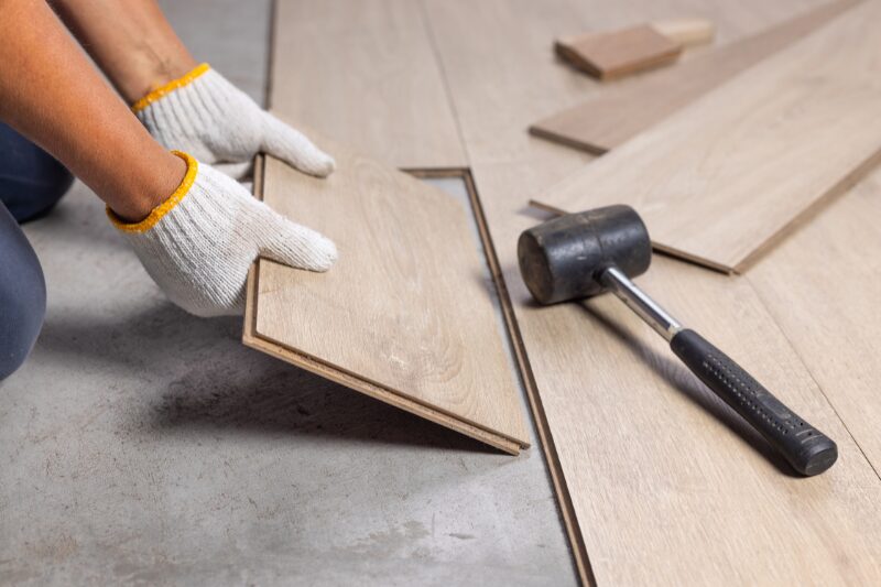 Persona con guanti da lavoro che posa un pavimento in legno durante la ristrutturazione di una casa.