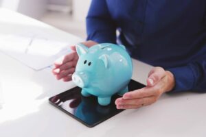 Persona che protegge un salvadanaio a forma di maialino azzurro appoggiato su un tablet, simbolo di risparmio e pensione integrativa digitale.