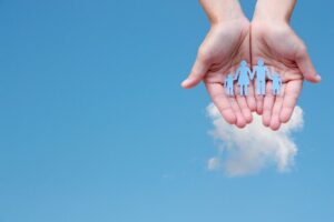 Mani che sorreggono sagome di carta azzurra raffiguranti una famiglia, simbolo di protezione, sicurezza e tutela assicurativa.
