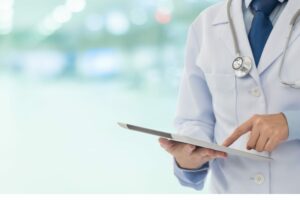 Medico in camice bianco utilizza un tablet per consultare informazioni cliniche.