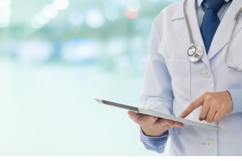 Medico in camice bianco utilizza un tablet per consultare informazioni cliniche.