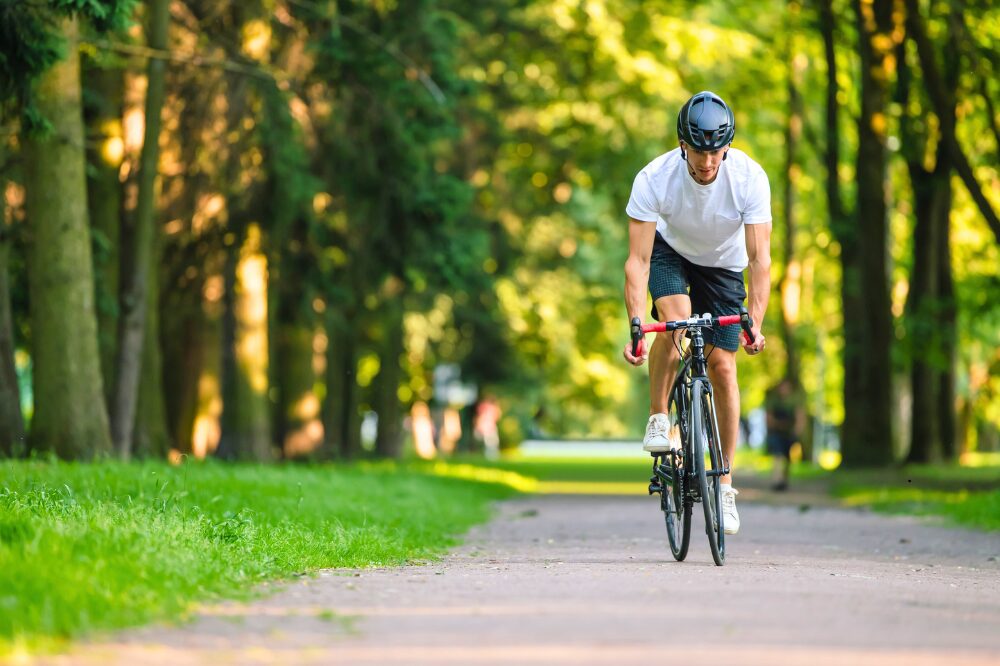 Ciclista adulto con casco che pedala su una pista ciclabile immersa nel verde in un parco urbano.