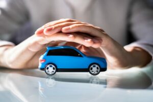 Mani di una persona che proteggono una piccola auto blu, simbolo di tutela e assicurazione del conducente.