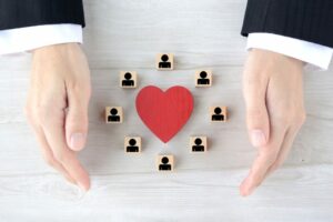 Mani che proteggono un cuore rosso circondato da icone di persone, simbolo di welfare aziendale, protezione dei dipendenti e benessere in azienda.